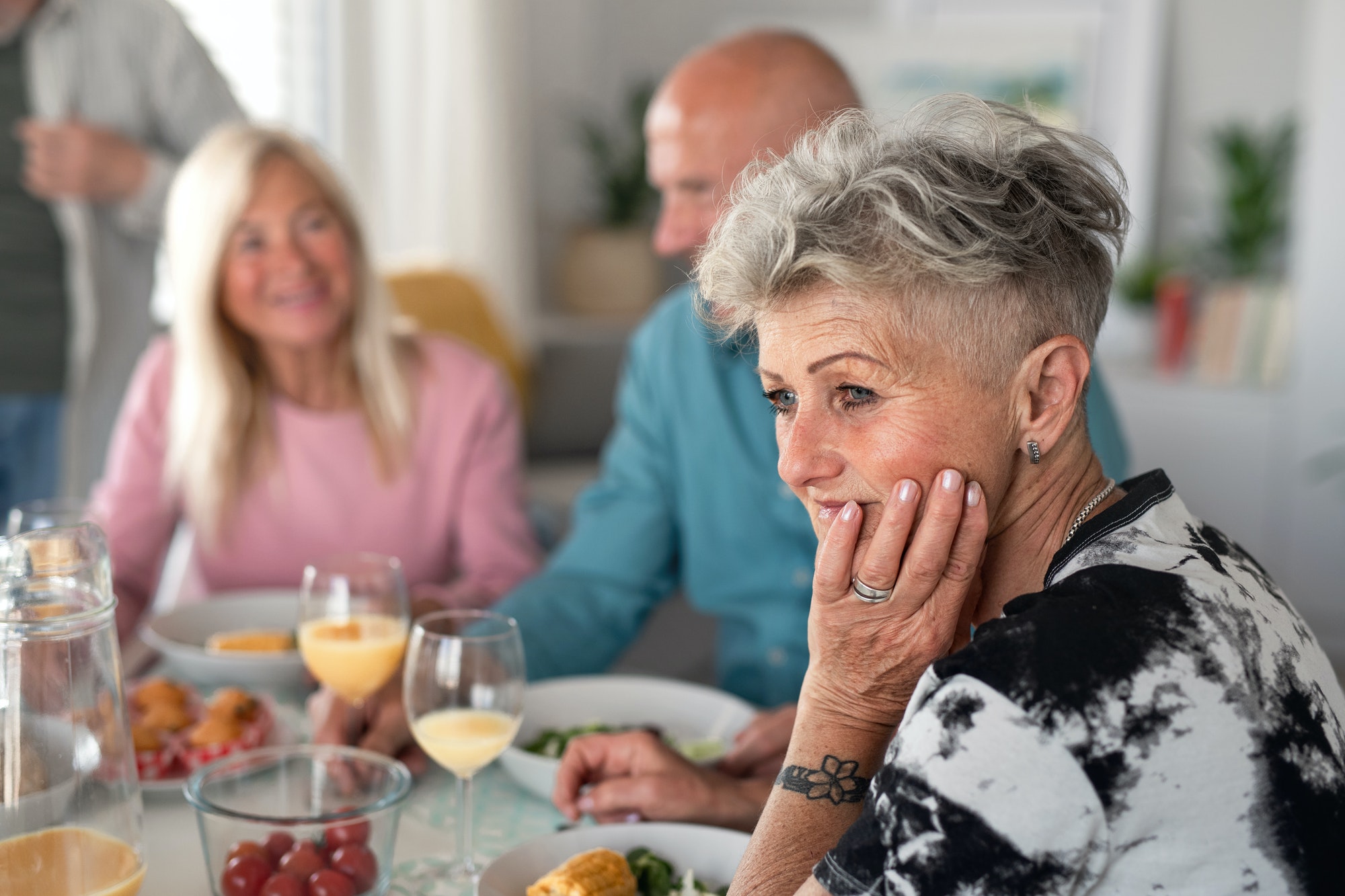 Sad senior woman with friends having party indoors, eating at the table